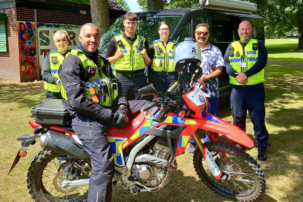 Cllr Almass stands with a group of PCSOs and an off road motorbike police officer in Cross Flatts Park